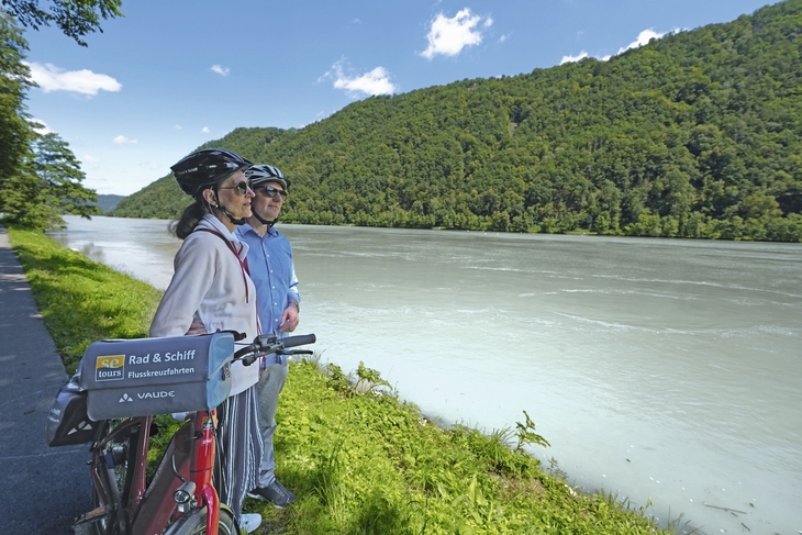 Zwei Radfahrer mit Helmen blicken auf die Donau entlang des Donauradwegs.