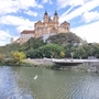 Stift Melk auf einem Hügel mit Donau im Vordergrund bei sonnigem Wetter.