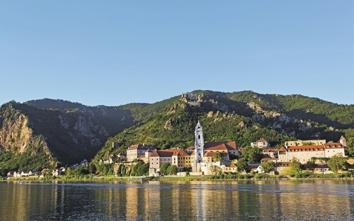 Stadt Dürnstein an der Donau mit Kirchturm und bewaldeten Hügeln im Hintergrund