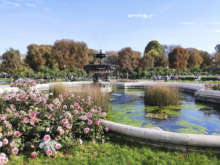 Brunnen in einem blühenden Park mit Herbstbäumen im Hintergrund.