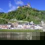 Blick auf die Reichsburg Cochem und den Fluss Mosel, umgeben von grüner Landschaft.