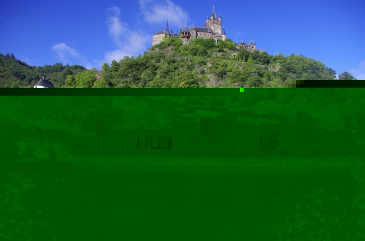 Blick auf die Reichsburg Cochem und den Fluss Mosel, umgeben von grüner Landschaft.