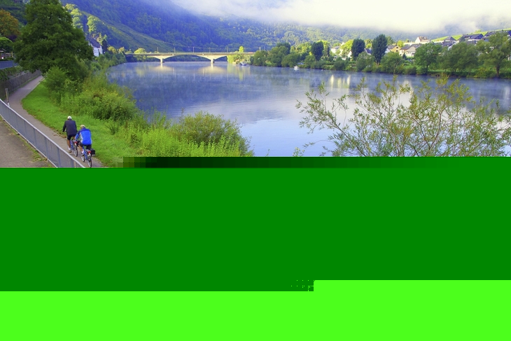 Radfahrer auf einem Weg entlang eines Flusses mit Brücke im Hintergrund.