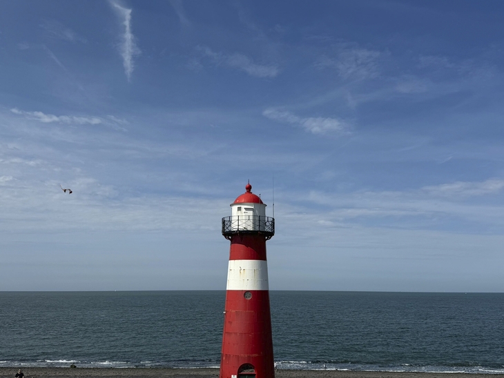 Roter Leuchtturm in Westkapelle vor blauem Himmel und Meer.