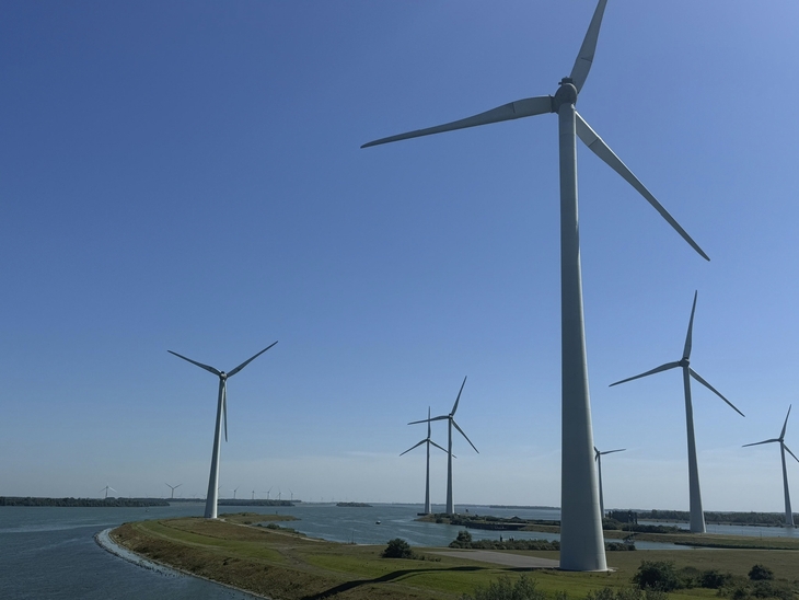 Windräder auf einem Deich in Zeeland, Niederlande bei klarem Himmel.