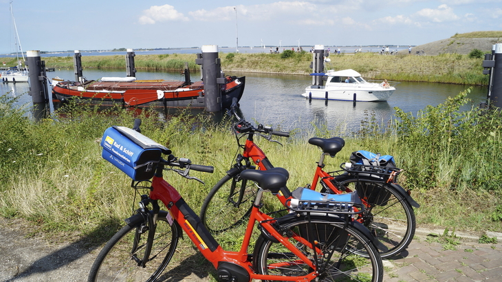 Rote Fahrräder am Wasser mit Booten im Hintergrund.