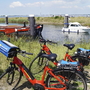 Rote Fahrräder am Wasser mit Booten im Hintergrund.