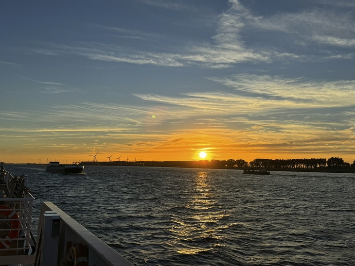 Sonnenuntergang über dem Meer mit Schiff und Windrädern im Hintergrund.