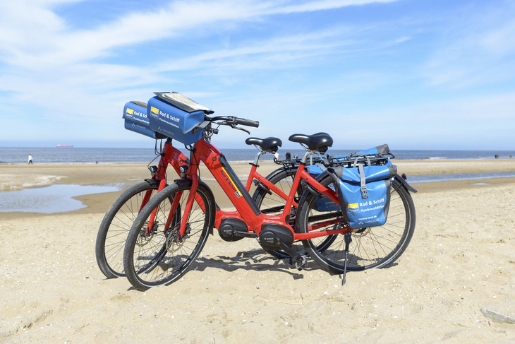 Zwei rote Fahrräder am Strand von Zeeland mit Meer im Hintergrund.