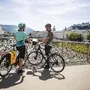 Zwei Radfahrer auf dem Makartsteg in Salzburg, Schloss im Hintergrund.