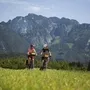Zwei Radfahrer vor einer Bergkulisse auf einem grünen Feld.