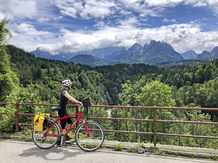 Radfahrer auf einer Straße mit Blick auf bewaldete Berge und bewölkten Himmel.