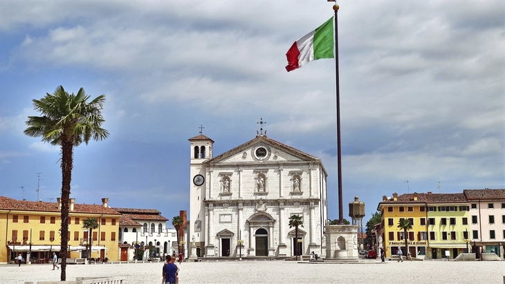 Historisches Gebäude in Udine mit italienischer Flagge im Vordergrund.