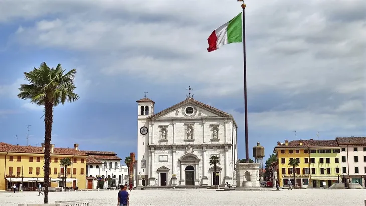 Historisches Gebäude in Udine mit italienischer Flagge im Vordergrund.