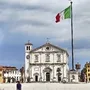 Historisches Gebäude in Udine mit italienischer Flagge im Vordergrund.