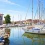 Boote im Hafen von Grado, umgeben von Gebäuden, unter blauem Himmel.