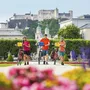 Drei Radfahrer im Mirabellgarten Salzburg mit Festung Hohensalzburg im Hintergrund.