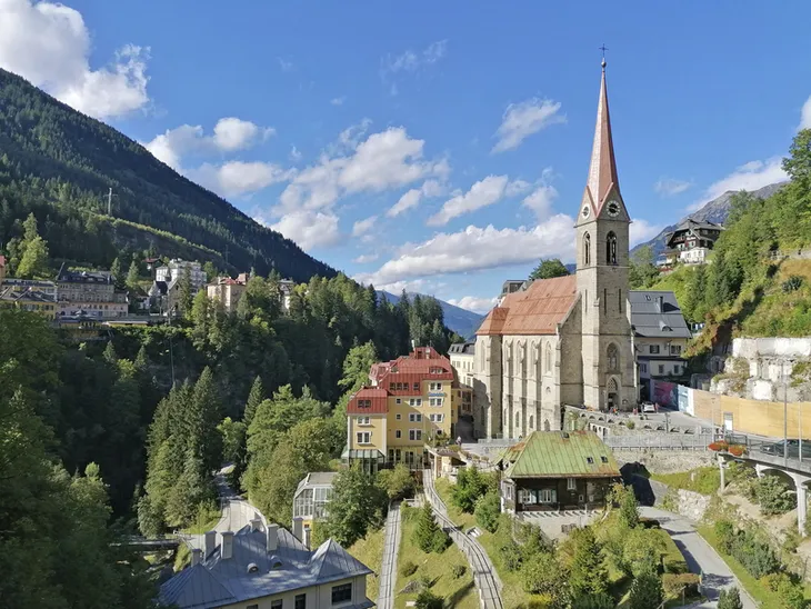 Kirche in Bad Gastein, umgeben von Bergen und Häusern unter blauem Himmel.