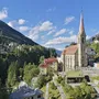 Kirche in Bad Gastein, umgeben von Bergen und Häusern unter blauem Himmel.