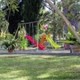 Spielplatz mit Rutsche und Schaukeln in grünem Garten umgeben von Bäumen.