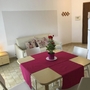 Esszimmer mit Tisch, roten Tischläufer, weißen Stühlen und Sofa im Hintergrund.