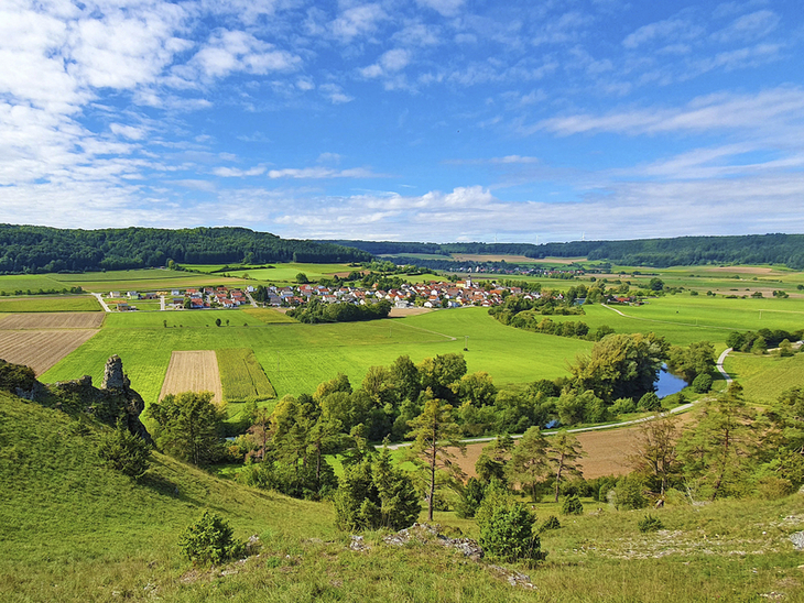 Panoramablick über grüne Landschaft und Dorf im Altmühltal an einem sonnigen Tag.