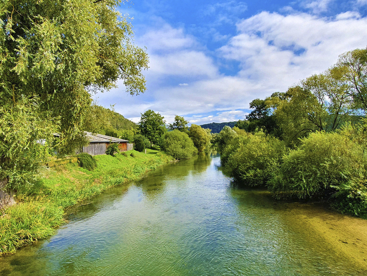 Blick auf Fluss und grüne Landschaft im Altmühltal unter blauem Himmel mit Wolken.