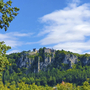 Blick auf eine Burg auf einem bewaldeten Felsen unter blauem Himmel im Altmühltal.