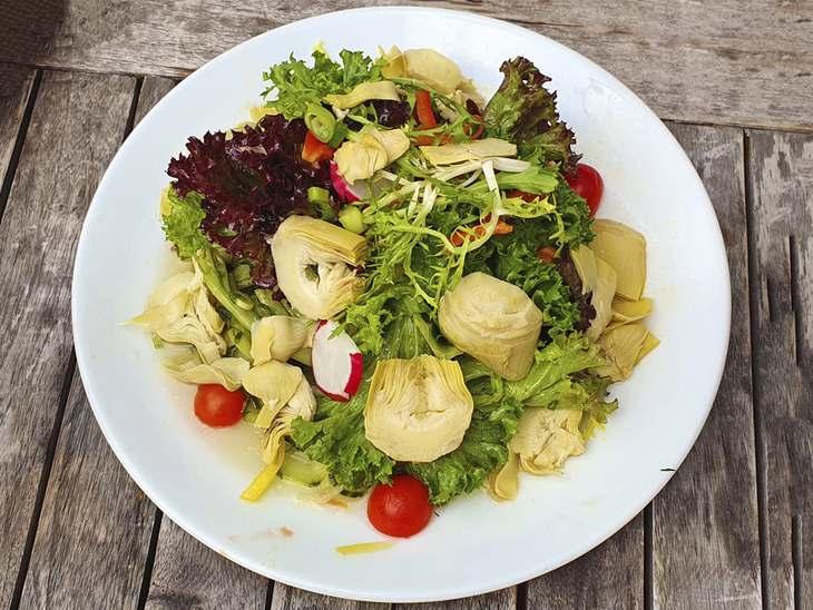 Teller mit frischem Salat, Artischockenherzen und Kirschtomaten auf Holztisch.