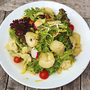 Teller mit frischem Salat, Artischockenherzen und Kirschtomaten auf Holztisch.