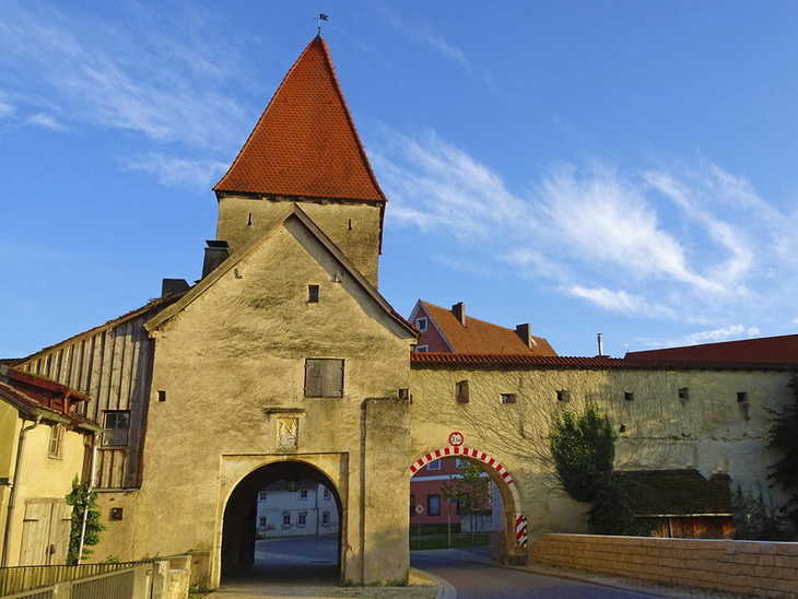 Historisches Stadttor mit rotem Dach und blauem Himmel im Hintergrund.