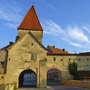 Historisches Stadttor mit rotem Dach und blauem Himmel im Hintergrund.