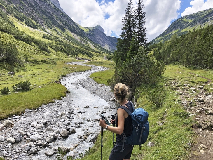 Wanderer blickt auf Fluss und Berge in alpiner Landschaft.