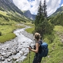 Wanderer blickt auf Fluss und Berge in alpiner Landschaft.