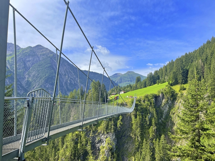 Hängebrücke in Holzgau, umgeben von alpiner Landschaft und grünen Wäldern.