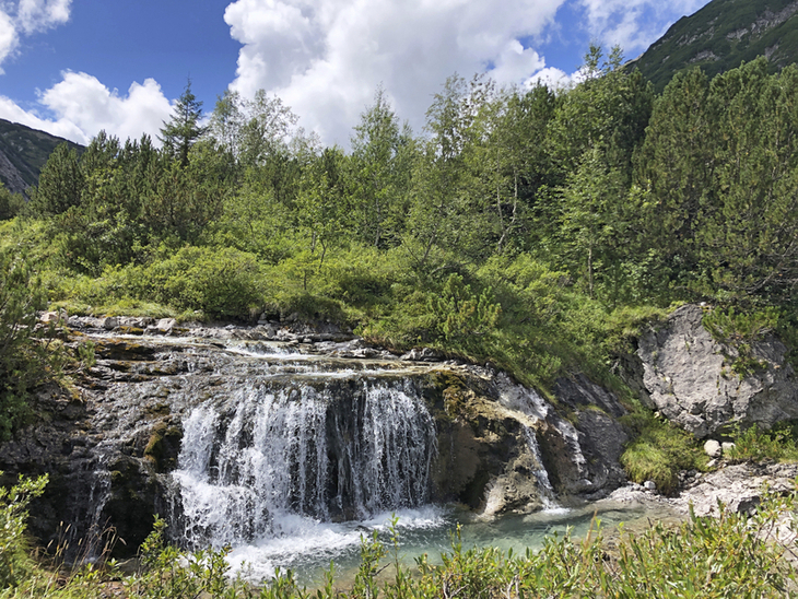 Wasserfall in einer grünen Waldlandschaft am Lechweg bei sonnigem Wetter.