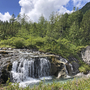 Wasserfall in einer grünen Waldlandschaft am Lechweg bei sonnigem Wetter.