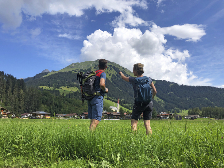 Wanderer mit Rucksäcken schauen auf eine Berglandschaft am Lechweg.
