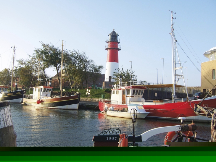 Boote im Hafen von Büsum vor einem Leuchtturm bei klarem Himmel.