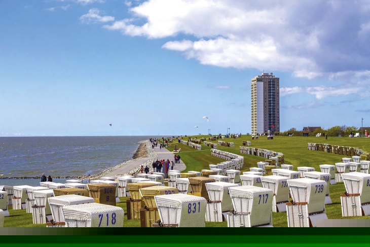 Viele Strandkörbe auf einer Wiese am Meer von Büsum, Hochhaus im Hintergrund, blauer, leichtbewölkter Himmel.