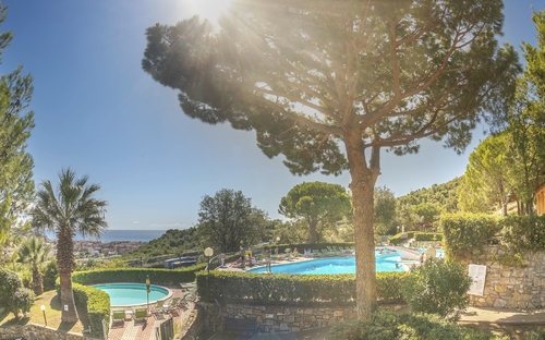 Swimmingpool und Bäume im Villaggio Colombo bei Sonnenschein.