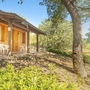 Bungalow im Grünen mit Terrasse und Stühlen, umgeben von Bäumen und Pflanzen.