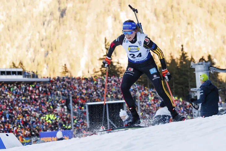 Biathlet im Rennen des Staffelwettbewerbs mit verschneiter Berglandschaft im Hintergrund.