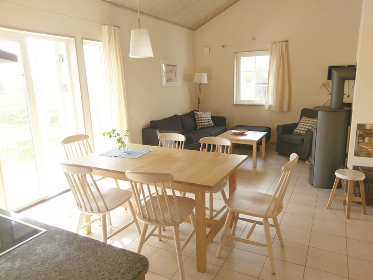 Helles Wohnzimmer mit Esstisch, Stühlen und Sofa, mit Blick ins Freie.