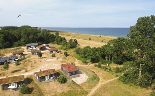 Blick auf ein Stranddorf mit grüner Landschaft und Meer im Hintergrund.