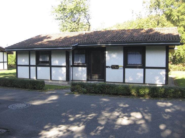 Kleines Fachwerkhaus im Ferienpark Ronshausen, umgeben von Bäumen, mit gepflastertem Weg.