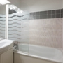 Badezimmer mit weißen Fliesen, Badewanne und Waschbecken.