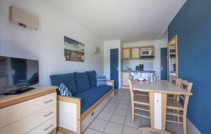 Wohnbereich mit Sofa, Esstisch, Küchenzeile und Wandbild in einem Apartment.
