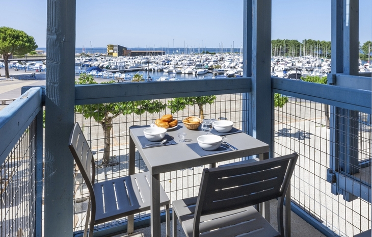 Balkon mit Tisch und Stühlen, Blick auf einen Yachthafen bei sonnigem Wetter.