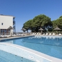 Poolbereich einer Ferienresidenz mit Sonnenliegen und Bäumen im Hintergrund.